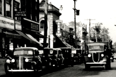 black and white photo of cars lined up outside a shop