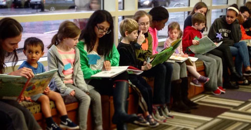 Photo of younger elementary school age kids practicing reading with teenagers