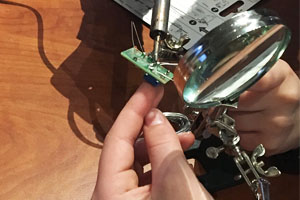 Hand holding a magnifying glass and soldering iron