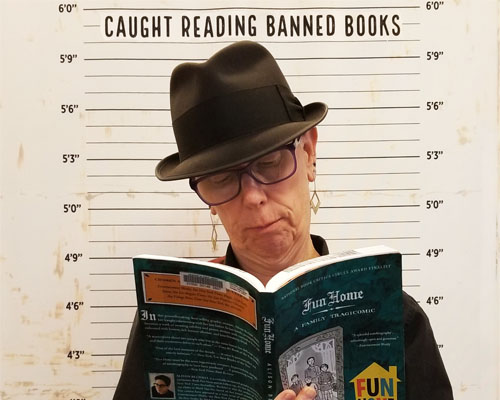 Library Director Diane Kresh standing in front of the 2017 Banned books Week display holding a copy of "Fun Home"