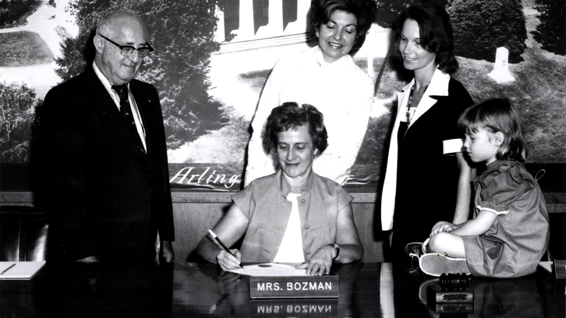 Ellen Bozman working in the County board room, surrounded by a man, two women and a child sitting on the desk