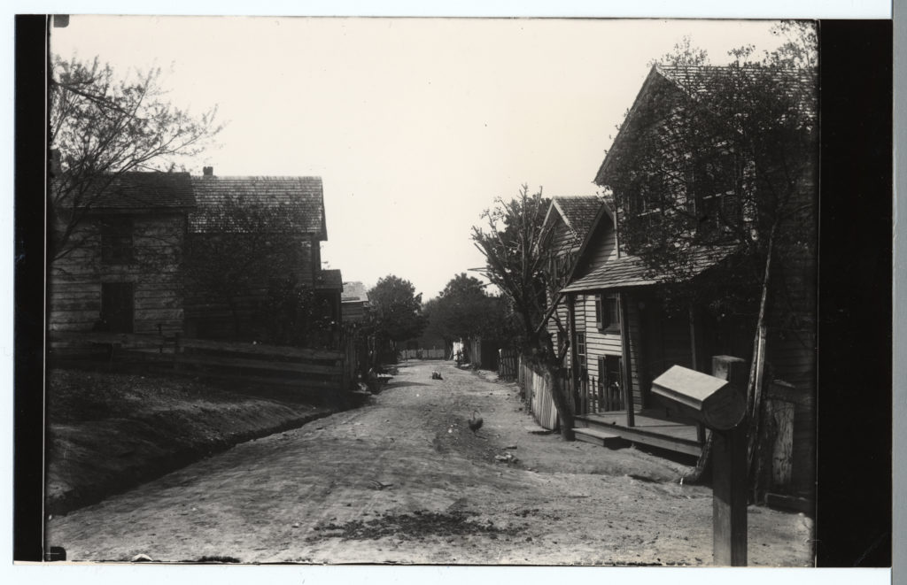 Black and white photo of wooden houses on a dirt road