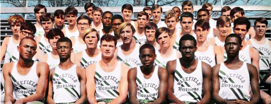 colorized photo of high school black and white boys sitting on the bleachers in track uniforms