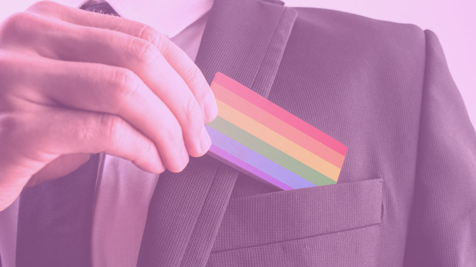 Man in a business suit slipping a rainbow card into his breast pocket