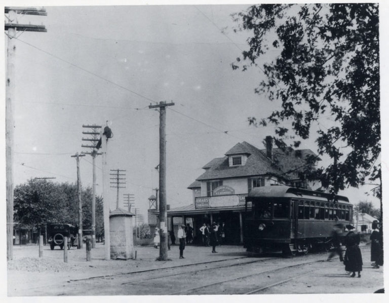 Black and white photo of trolley station with trolley to the right of the building