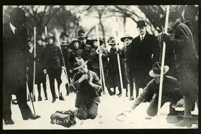 Young Carl Porter kneels in front of a row a Scouts to demonstrate fire building