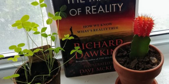 My years-old cactus is lately becoming friends with a recent household addition, some red clover. Together they are sharing in The Magic of Reality by Dawkins.
