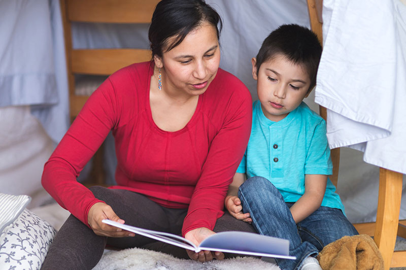 Native American mom reads with her son under makeshift fort in living room