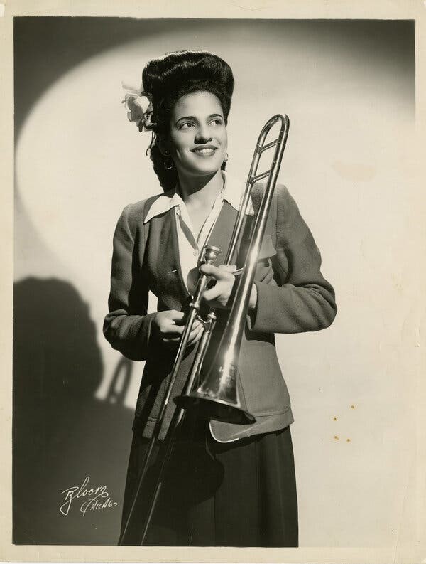 A woman holds a trombone and smiles.
