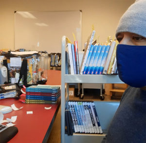 Man wearing a mask, surrounded by DVDs and books.