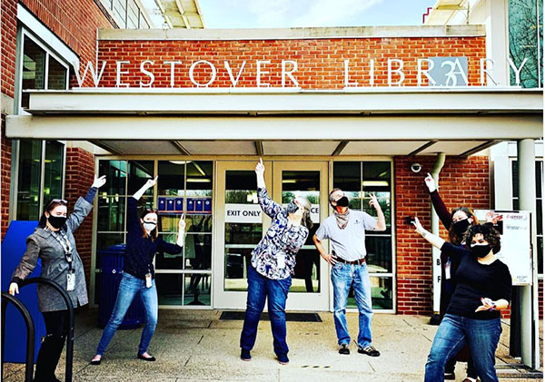 Library staff stand outside of Westover pointing at the front door, looking excited.
