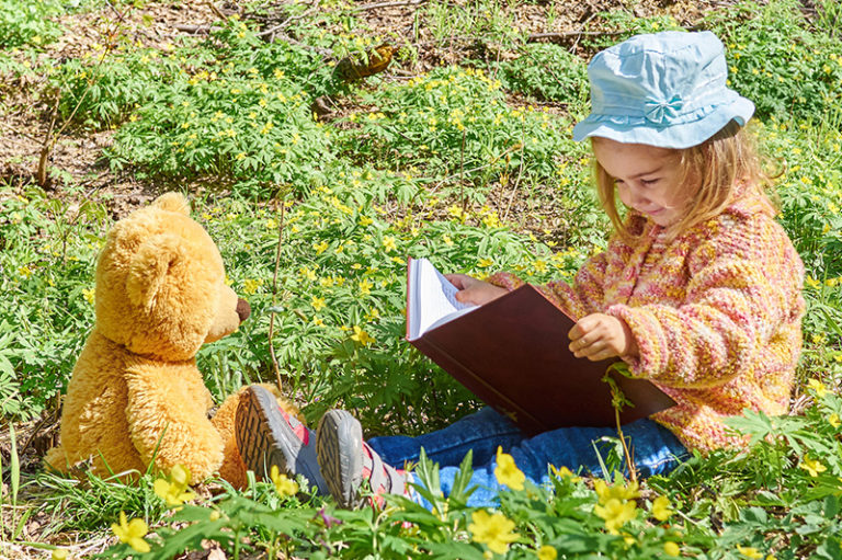 Young child reading to her teddy bear outside in the park.