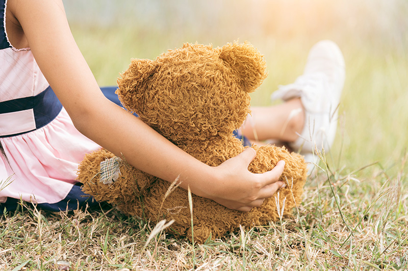 Young girl holding a teddy bear while sitting outside in the park.