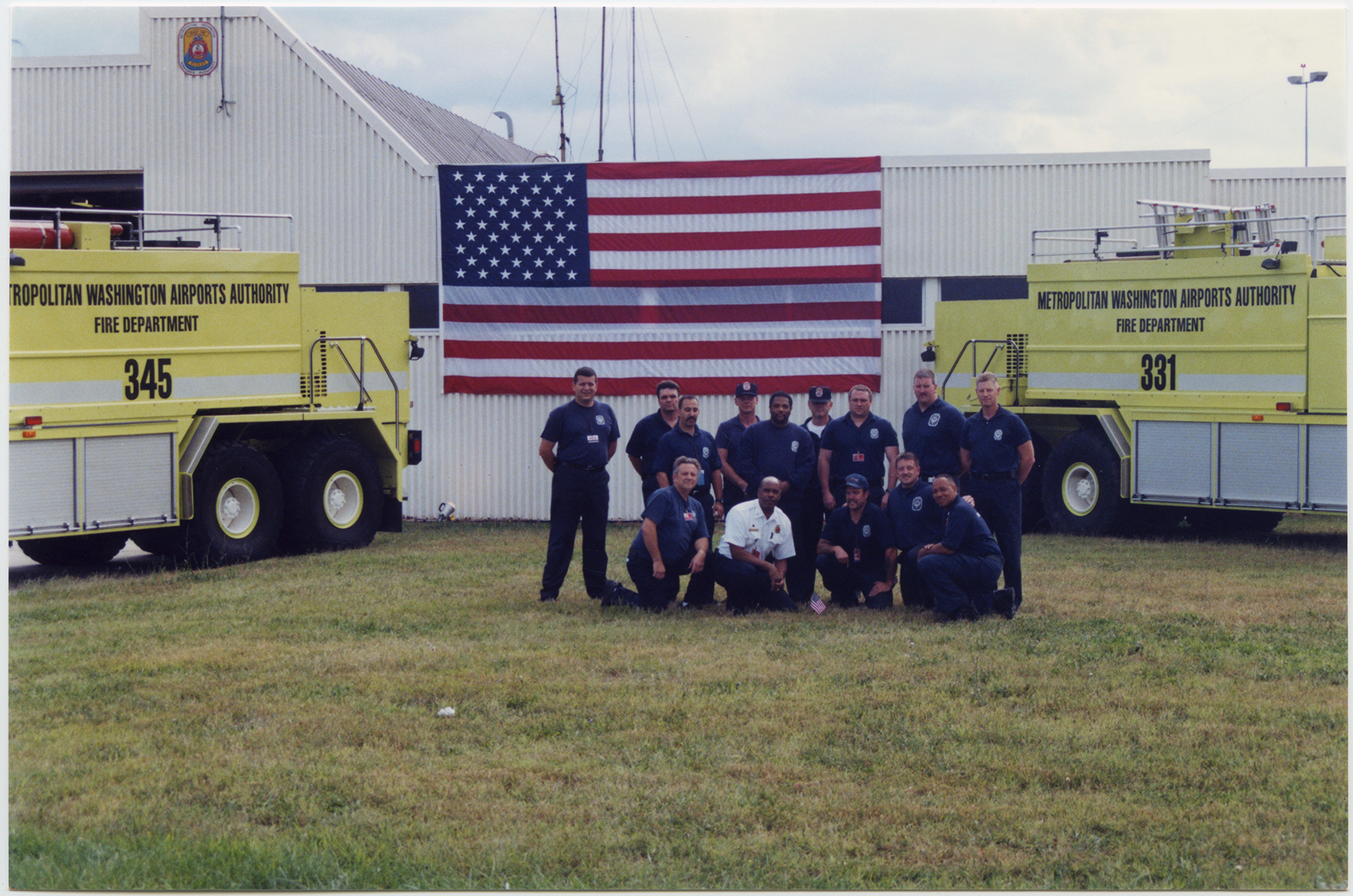 The two foam units, along with their crews, that were on the original call to the Pentagon on September 11, parked in front of the American flag displayed on the front of the National Airport fire station. 2001, 1 print, col., 4 x 6 in..