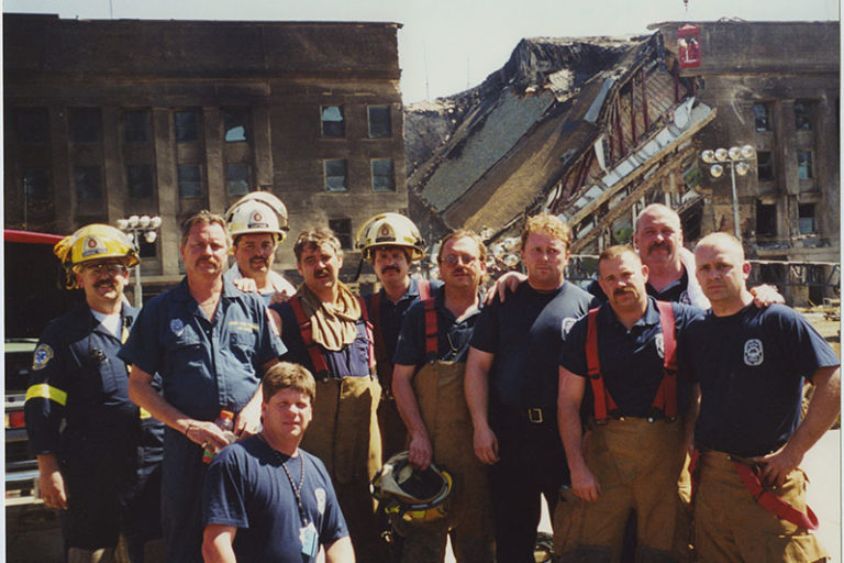 Firefighters stand in front of the burned and broken Pentagon.