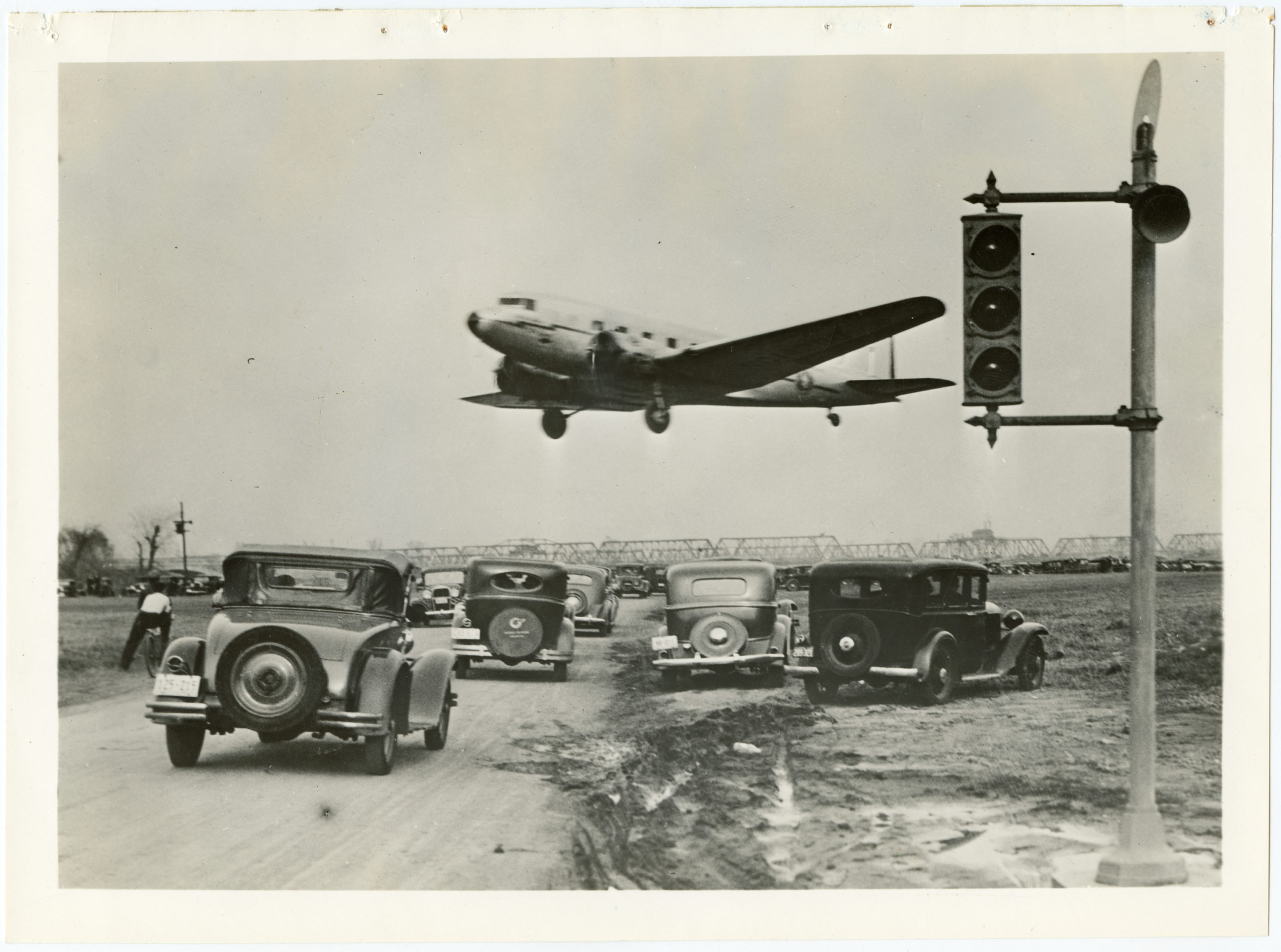 A passenger plane flying low over several cars. 1930, 1 print, b&amp;w, 7.5 x 10 in..