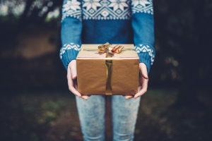 Person with blue sweater holding a brown paper-wrapped gift.