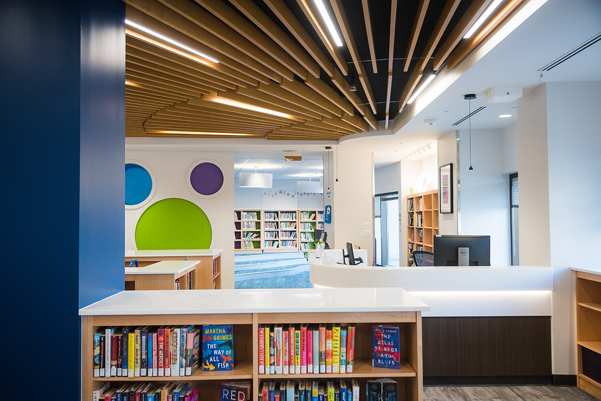 The librarian's desk at Courthouse Library, with a blue support beam to the left, colorful painted circles decorating the wall, and shelves filled with books in the foreground and background.