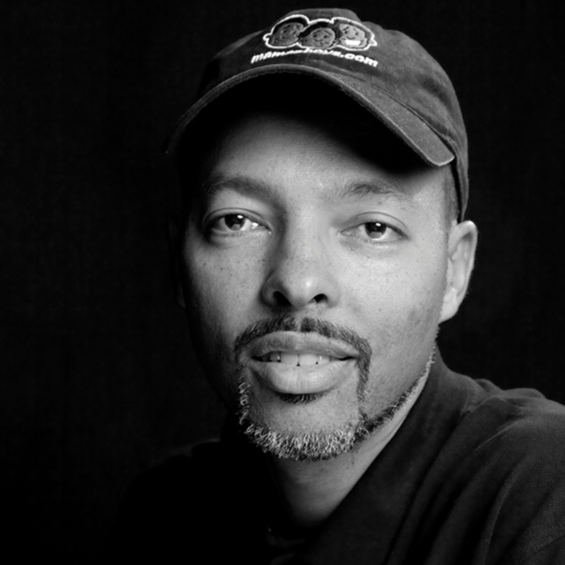 Headshot of author Jerry Craft, wearing a baseball cap featuring characters from his graphic novels.