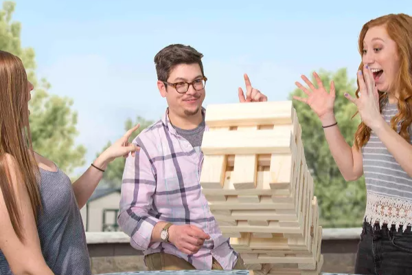 Three people smile and laugh as a jenga tower falls
