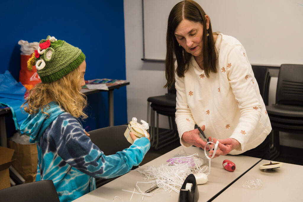 A volunteer helps a child wrap a present.