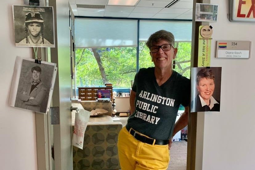 Diane Kresh stands in her office doorway wearing an Arlington Public Library t-shirt. Pictures from across her career are pinned to the doorway.