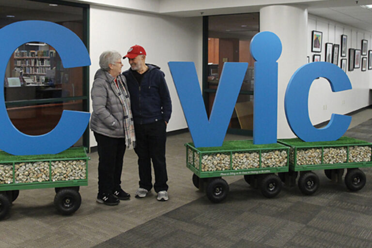 Photo of a couple standing in between a public sculture with the letters "Cvic." The couple is forming the letter "i"