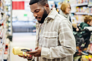 Man holds coffee bag in a store aisle while looking at his phone, which is held in his other hand.