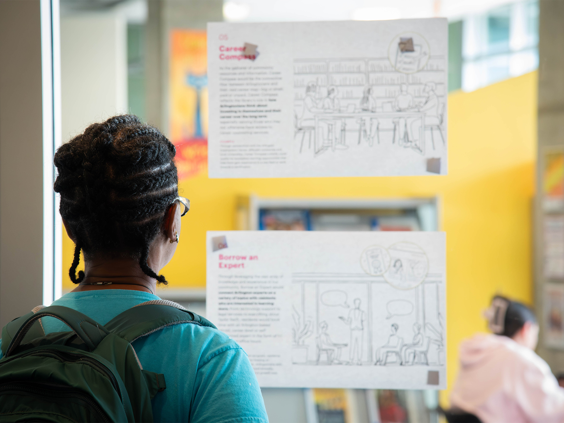 A patron views two Future of Libraries concept posters on the glass wall inside Shirlington Library.