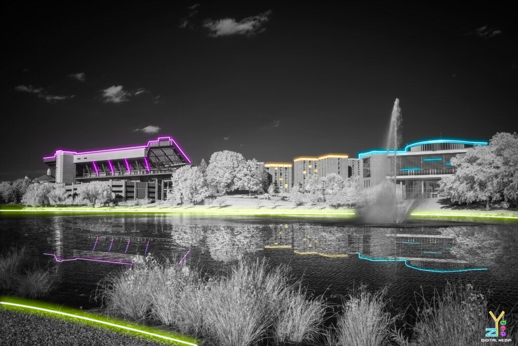 a football stadium and buildings in neon across the lake in black.