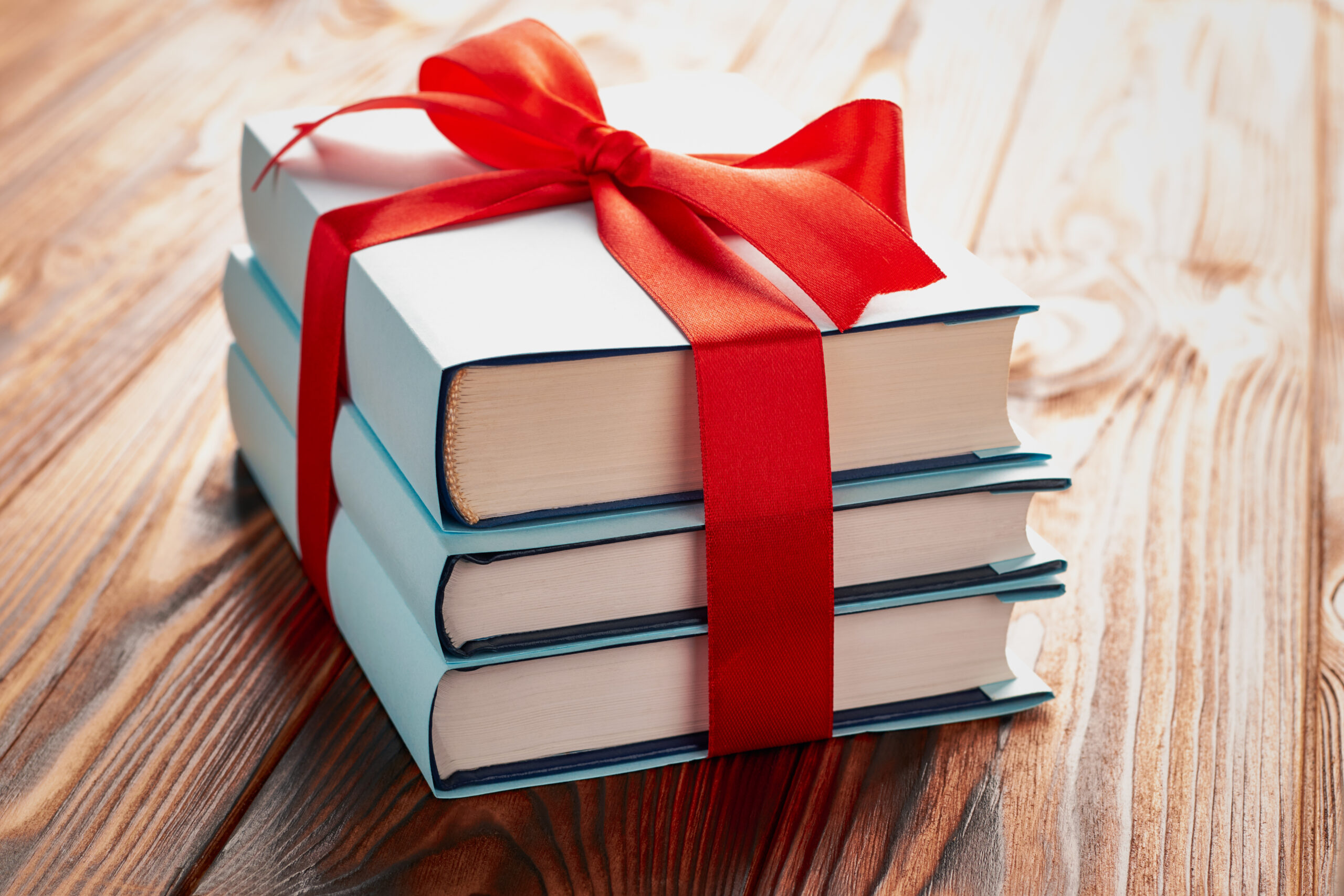 A stack of books tied together with a festive red gift bow on a wooden surface.