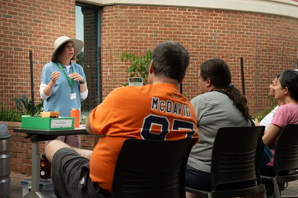 A garden educator speaking outdoors at Central Library while attendees sit and listen in front of the vegetable beds.