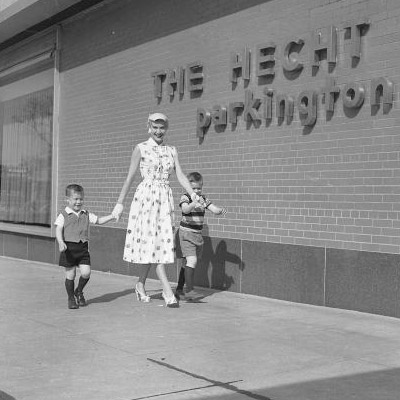 A women and two children walk in front of the Hecht's Parkington sign, posing for a photo.