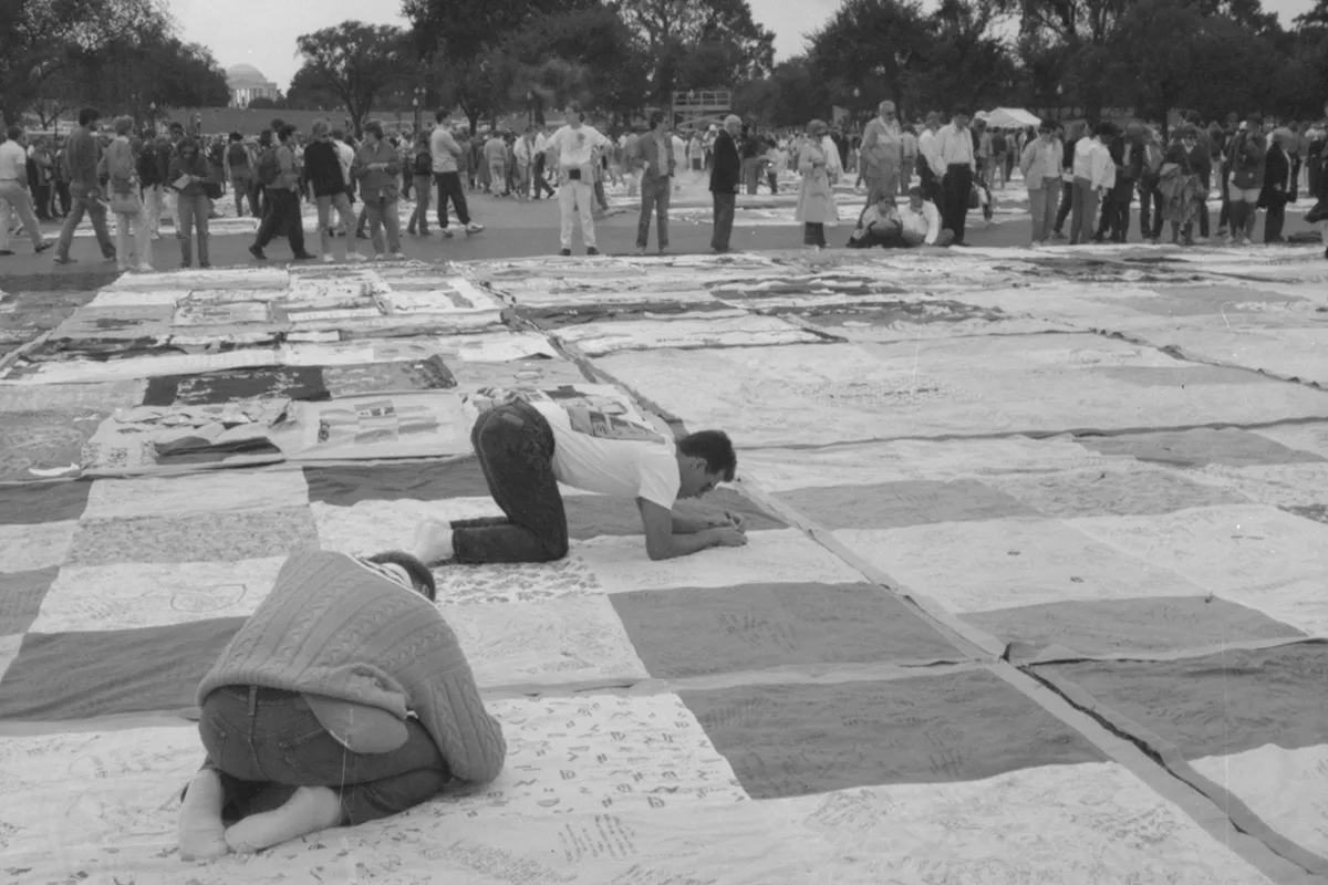 Three men writing on squares of the AIDS Quilt.