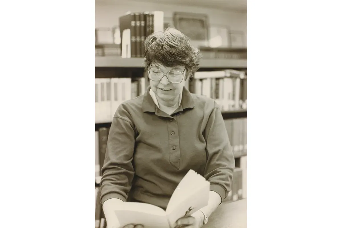 Sara Collins sitting a table reading a book. Bookshelves behind her.