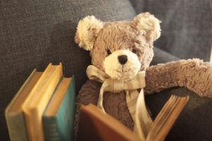 A teddy bear sitting in an arm chair reading a book.