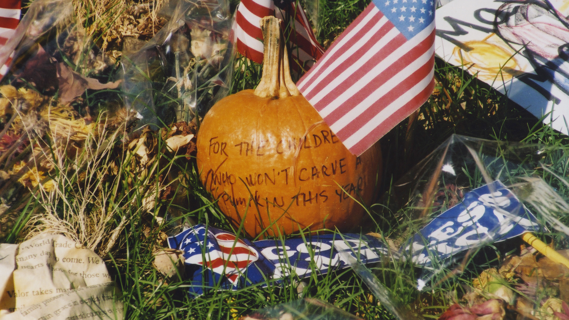 Closeup of a "God Bless America" bumper sticker and a pumpkin that has "For the children who won't carve a pumpkin this year" written on it, among the items at a memorial for the victims of the 9/11 terrorist attack on the Pentagon. Photo credit Diane Kresh. Charlie Clark Center for Local History,133-01-02-01-128