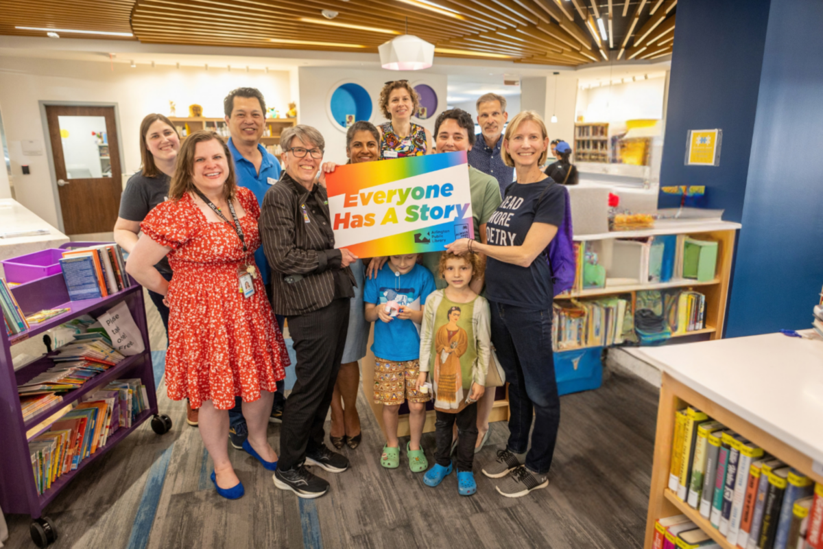 A group of smiling people hold a big library card that reads Everyone Has A Story.