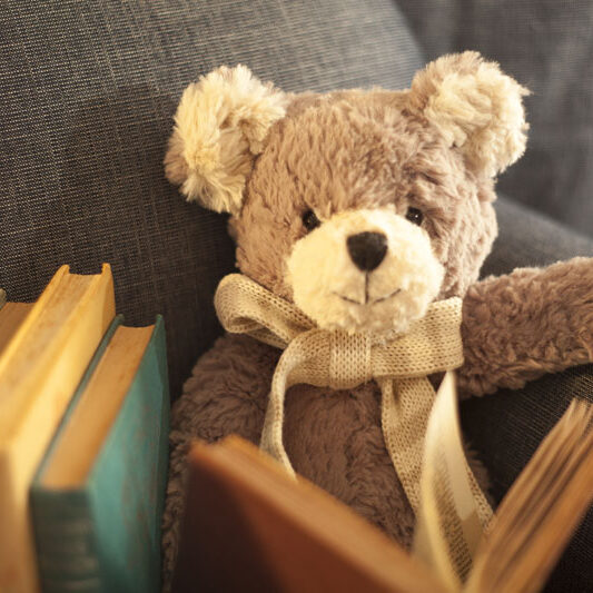 A teddy bear sitting in an arm chair reading a book.