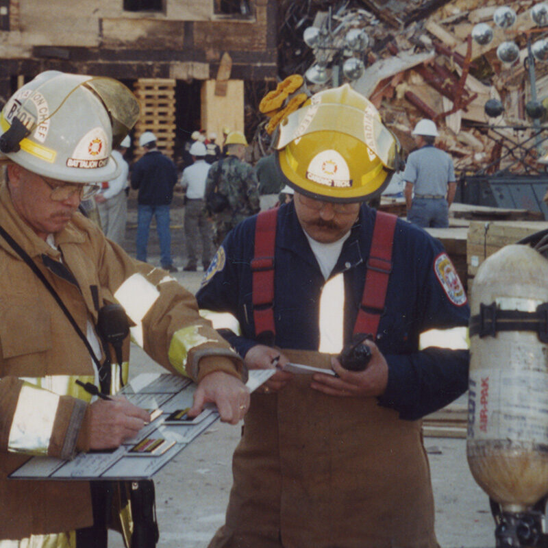Firefighters Planning Next Steps Two firefighters draw plans to work on the impact site at the Pentagon following the 9/11 attack. Photo credit Michael Defina. Charlie Clark Center for Local History, 133-0030