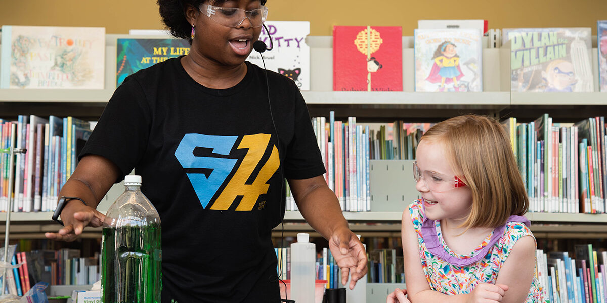 Photo of performer Talewise conducting a dish soap experiment with a young child helping her.